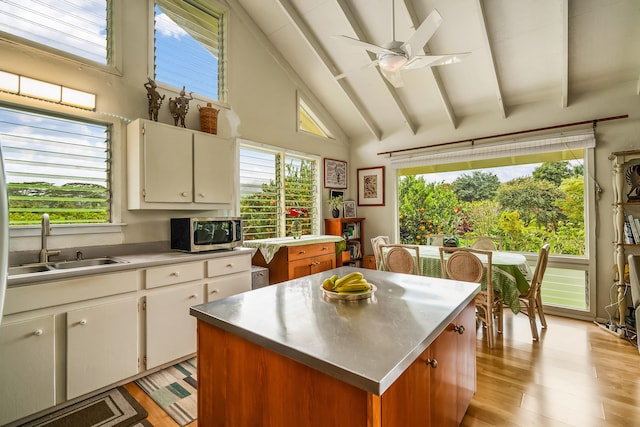 kitchen with stainless steel counters, stainless steel microwave, beam ceiling, a sink, and a wealth of natural light