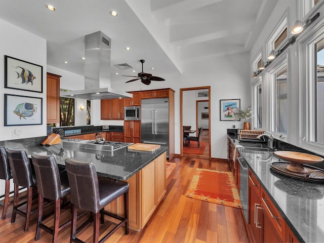 kitchen with visible vents, island exhaust hood, a kitchen breakfast bar, a peninsula, and built in appliances