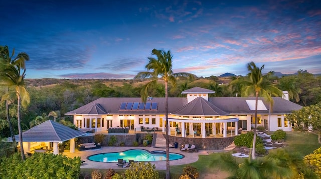 back of property at dusk with a gazebo, an outdoor pool, roof mounted solar panels, and a patio area