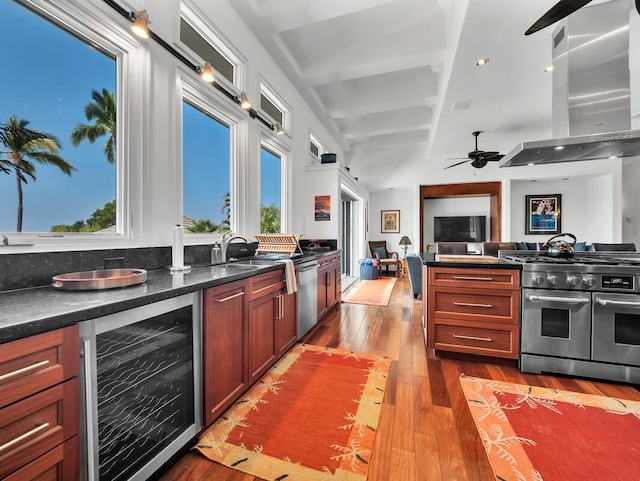 kitchen featuring beverage cooler, beamed ceiling, hardwood / wood-style floors, stainless steel appliances, and wall chimney exhaust hood