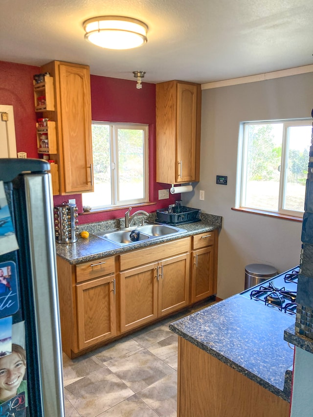 kitchen with a sink, gas cooktop, dark countertops, freestanding refrigerator, and brown cabinetry