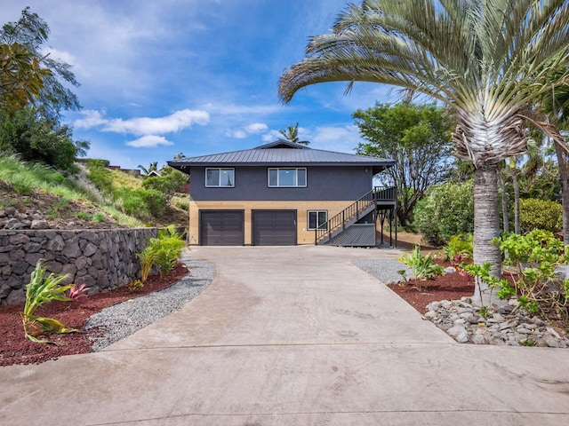 view of front facade with stucco siding, stairway, metal roof, concrete driveway, and a garage