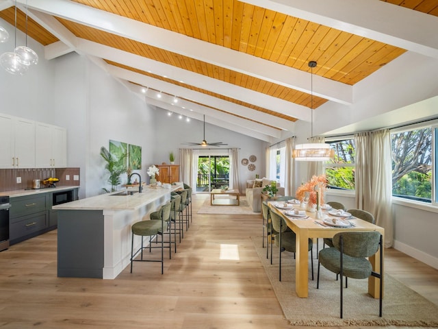 dining space with beam ceiling, baseboards, light wood-type flooring, and a wealth of natural light