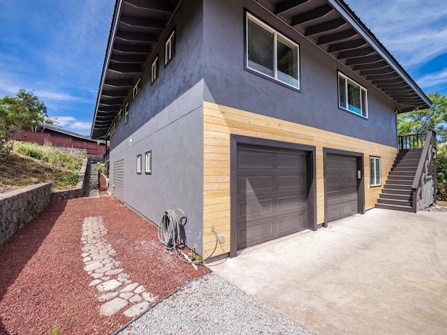 view of side of property featuring stucco siding, driveway, stairs, and an attached garage