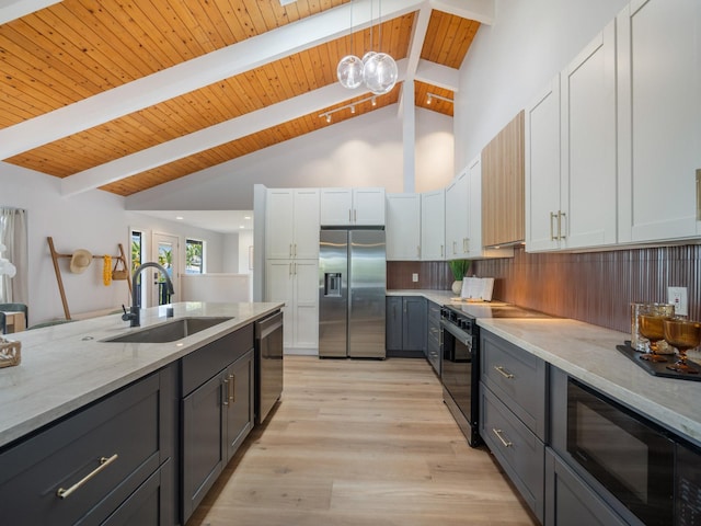 kitchen with beam ceiling, light wood-style flooring, a sink, appliances with stainless steel finishes, and backsplash