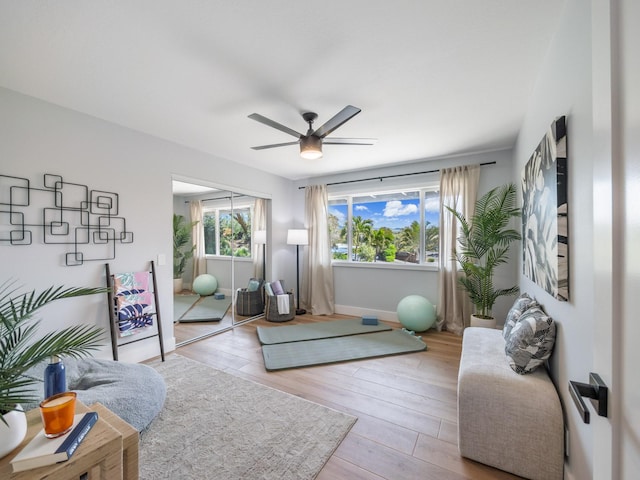 living area featuring wood finished floors, a healthy amount of sunlight, baseboards, and ceiling fan