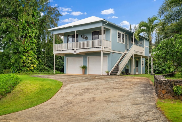 coastal home featuring a front yard, stairway, stucco siding, concrete driveway, and a garage