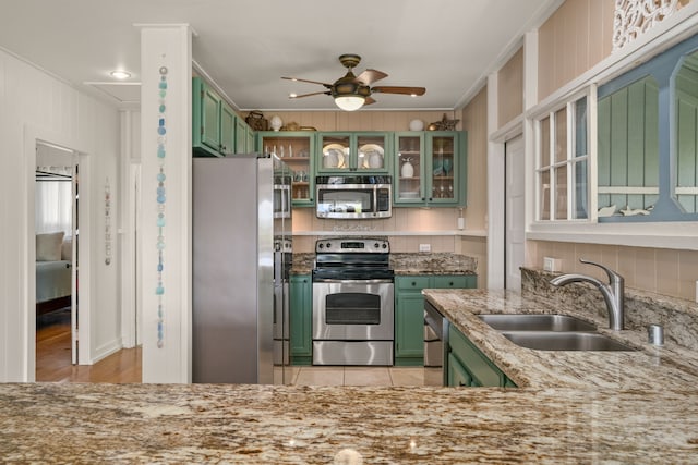 kitchen featuring a ceiling fan, a sink, appliances with stainless steel finishes, green cabinets, and light stone countertops