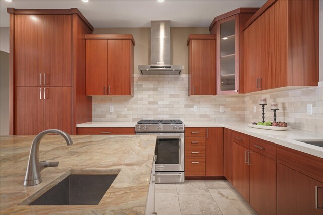 kitchen featuring wall chimney exhaust hood, glass insert cabinets, a sink, backsplash, and gas stove