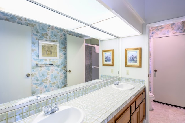 bathroom featuring wallpapered walls, a sink, toilet, and double vanity