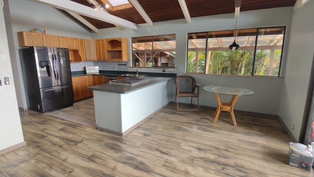 kitchen featuring a peninsula, vaulted ceiling with beams, dark countertops, refrigerator with ice dispenser, and backsplash