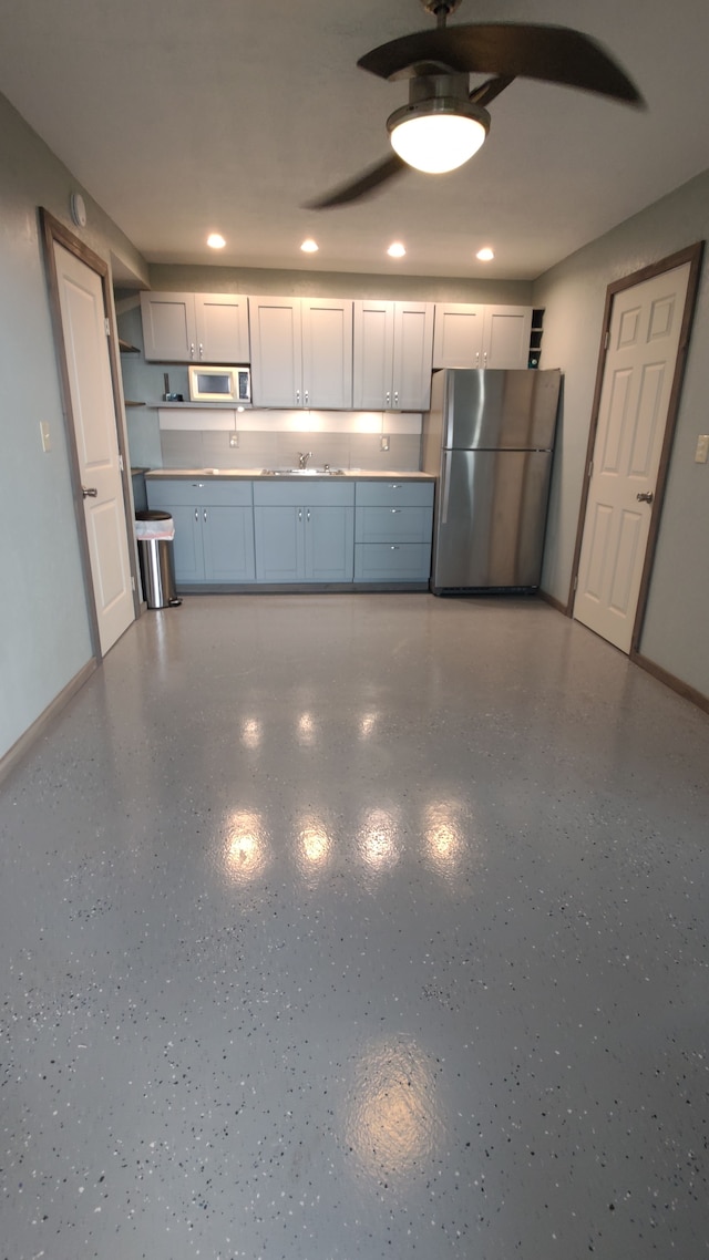 kitchen featuring white microwave, baseboards, ceiling fan, freestanding refrigerator, and a sink