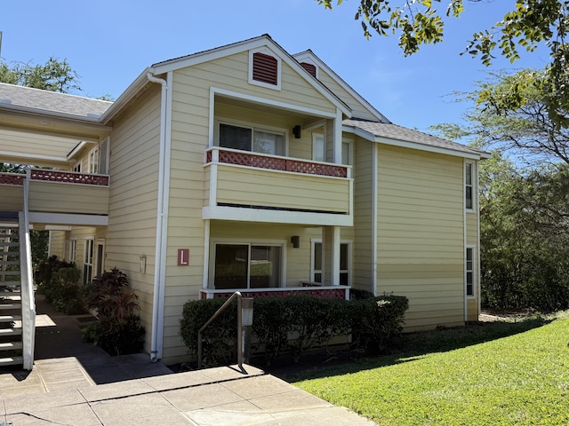 view of front of property featuring a balcony, stairway, and a front yard