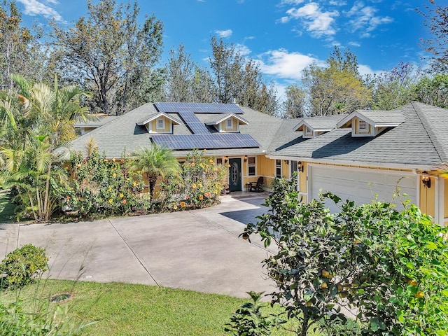 view of front of property featuring driveway, roof with shingles, solar panels, and an attached garage