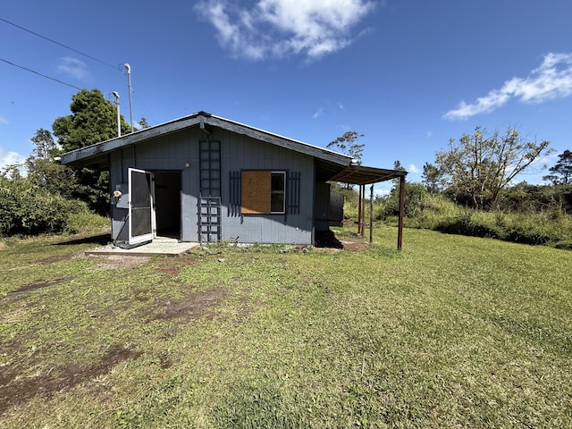 rear view of property featuring a carport, an outbuilding, and a yard