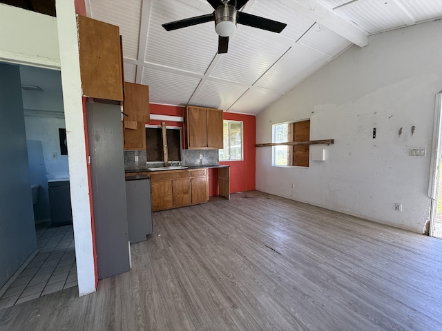 kitchen with dishwashing machine, brown cabinetry, lofted ceiling with beams, light wood-style flooring, and decorative backsplash