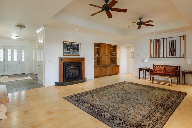 living room with wood finished floors, a tray ceiling, ceiling fan, a fireplace with raised hearth, and ornamental molding