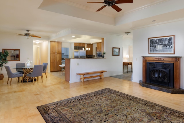 living area with light wood finished floors, crown molding, a ceiling fan, and a raised ceiling