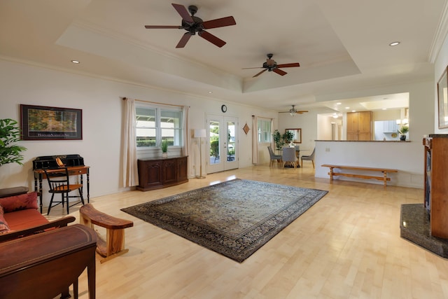 living area featuring a tray ceiling, crown molding, light wood-style flooring, and ceiling fan