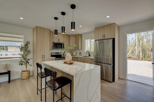 kitchen featuring stainless steel appliances, a sink, a breakfast bar area, light stone countertops, and light brown cabinets