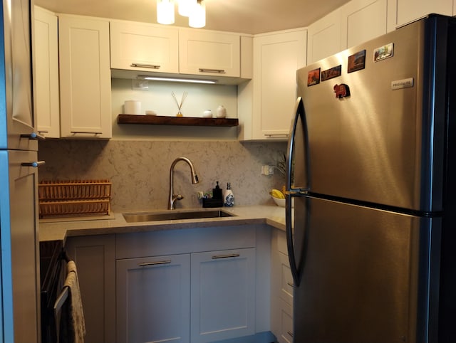 kitchen with a sink, open shelves, freestanding refrigerator, white cabinets, and decorative backsplash