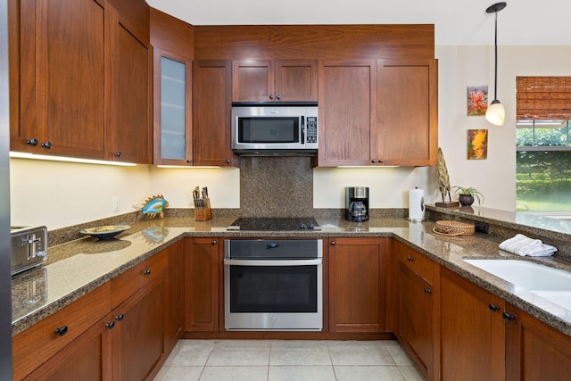 kitchen featuring decorative light fixtures, dark stone countertops, stainless steel appliances, light tile patterned flooring, and glass insert cabinets