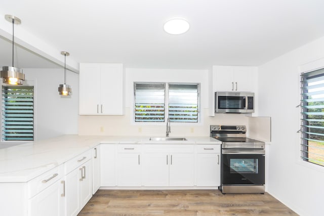 kitchen with a sink, stainless steel appliances, a peninsula, and white cabinetry