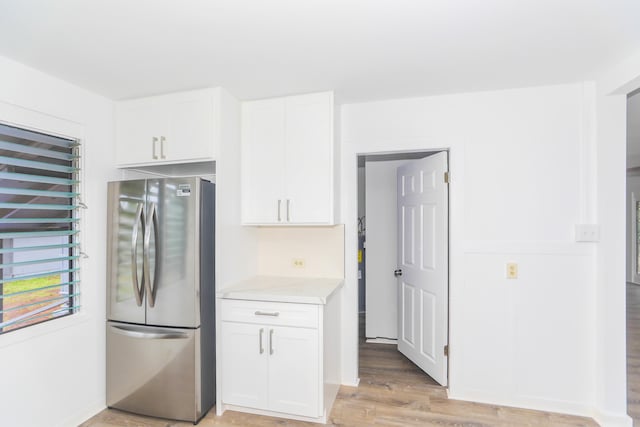 kitchen featuring backsplash, light stone counters, light wood-style flooring, freestanding refrigerator, and white cabinets