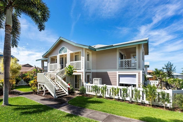 view of front facade with a fenced front yard, a porch, stairs, a front yard, and a balcony