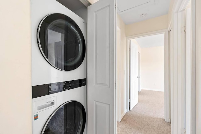 clothes washing area featuring baseboards, light colored carpet, laundry area, and stacked washer / dryer