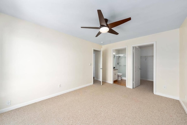 unfurnished bedroom with baseboards, ensuite bath, a closet, light carpet, and a walk in closet