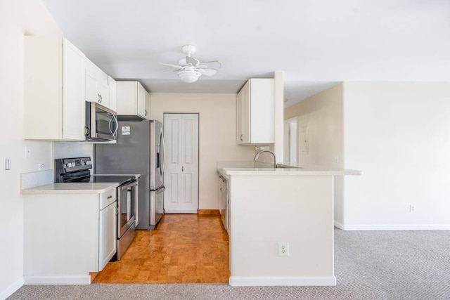 kitchen with ceiling fan, light carpet, appliances with stainless steel finishes, a peninsula, and white cabinets