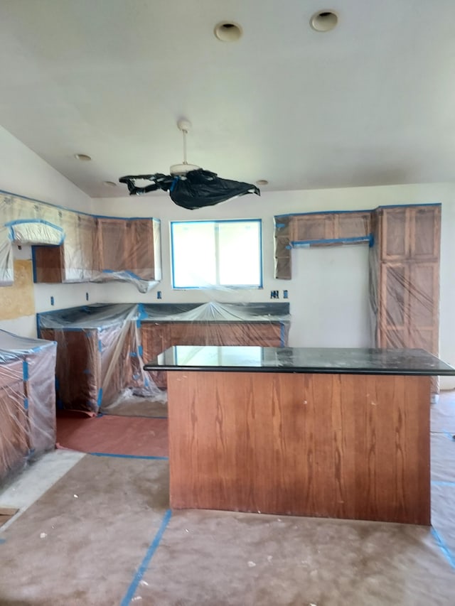 kitchen with brown cabinets, dark countertops, concrete floors, and vaulted ceiling