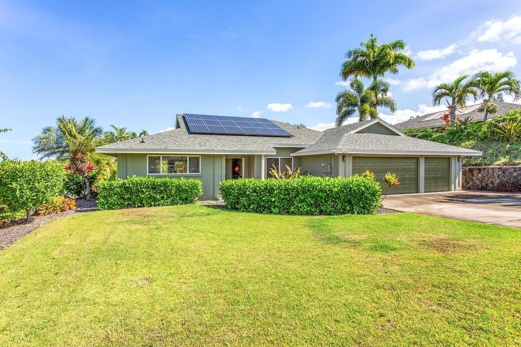 ranch-style home featuring a front yard, driveway, roof with shingles, solar panels, and a garage