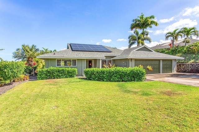 ranch-style home featuring a front yard, driveway, roof with shingles, solar panels, and a garage