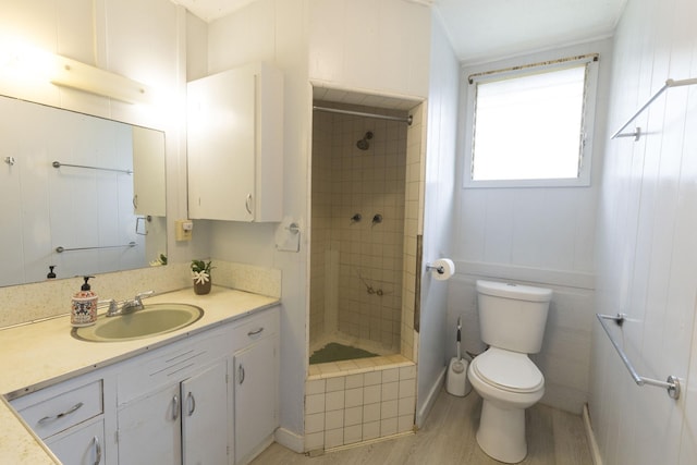 bathroom with vanity, toilet, wood finished floors, and tiled shower