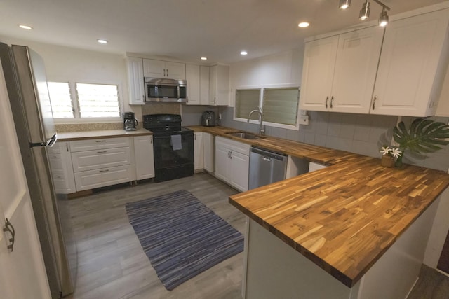 kitchen with wood counters, a sink, white cabinetry, and stainless steel appliances