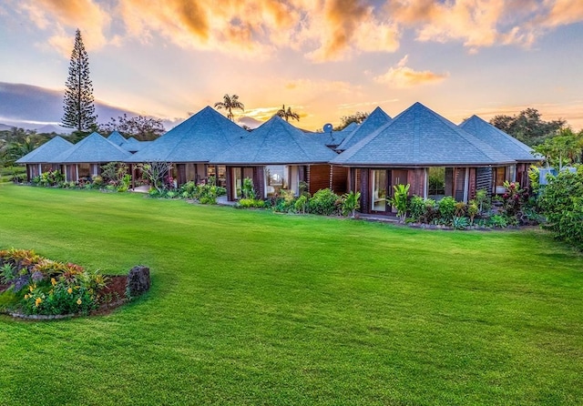 back of house at dusk featuring a lawn