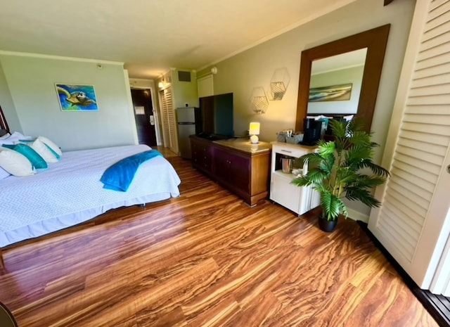bedroom with crown molding, wood finished floors, visible vents, and freestanding refrigerator