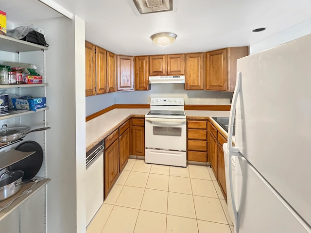 kitchen with under cabinet range hood, brown cabinetry, white appliances, and light tile patterned floors