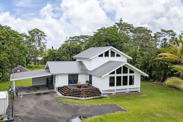 rear view of property featuring french doors, a lawn, a carport, driveway, and view of scattered trees