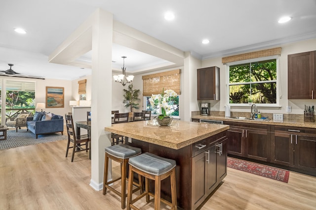 kitchen featuring a breakfast bar area, crown molding, light wood-style floors, and dark brown cabinets