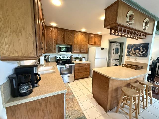 3880 Wyllie Rd Unit 8C, Princeville, HI 96722 - kitchen with stainless steel appliances, stacked washer / dryer, a breakfast bar, light countertops, and light tile patterned floors