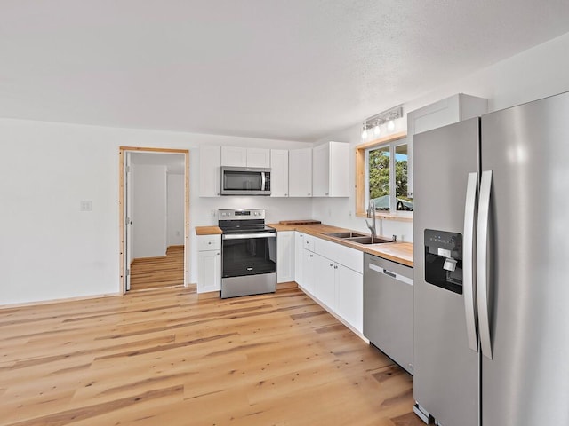 kitchen featuring a sink, light wood-type flooring, appliances with stainless steel finishes, white cabinetry, and wood counters