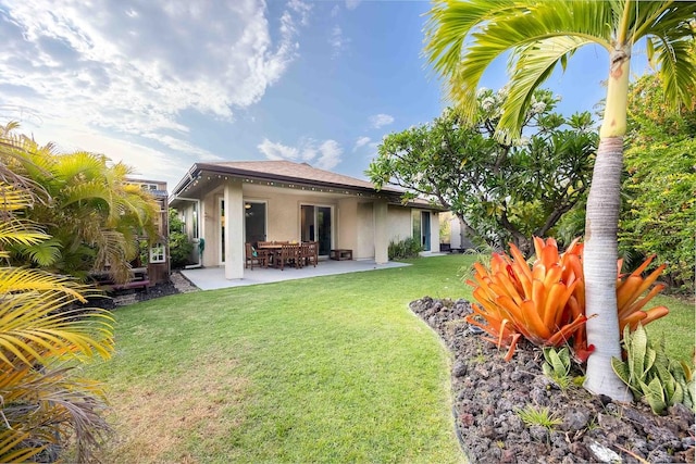 rear view of property with stucco siding, a yard, and a patio area