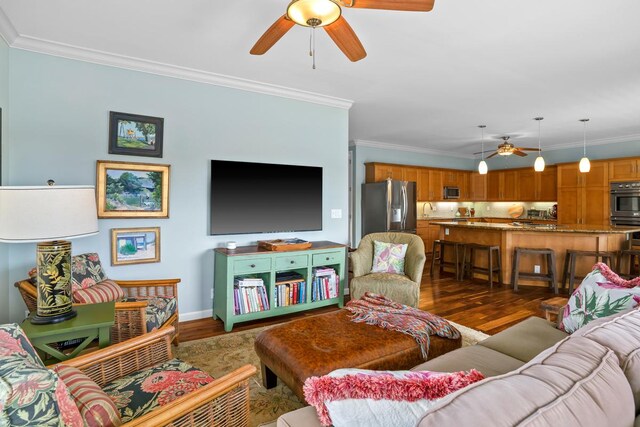 living area featuring dark wood-type flooring, ceiling fan, baseboards, and ornamental molding