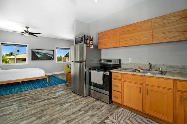 kitchen with stainless steel appliances, a sink, a ceiling fan, light stone countertops, and wood finished floors
