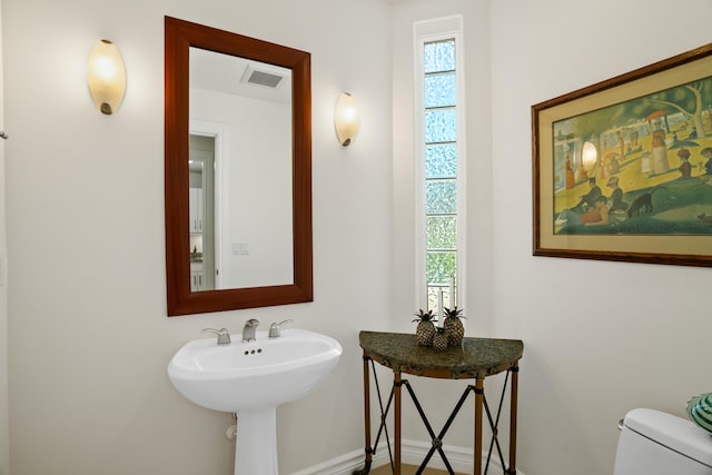 half bath with toilet, plenty of natural light, a sink, and visible vents