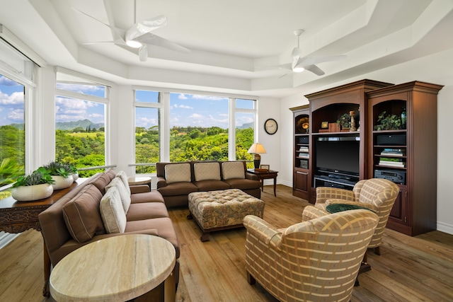 living area featuring a raised ceiling, hardwood / wood-style flooring, baseboards, and ceiling fan