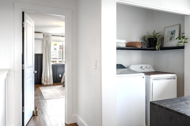 laundry area featuring a wall unit AC, baseboards, washing machine and dryer, laundry area, and wood finished floors